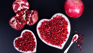 Pomegranate seeds in a shape of a heart on wooden background.