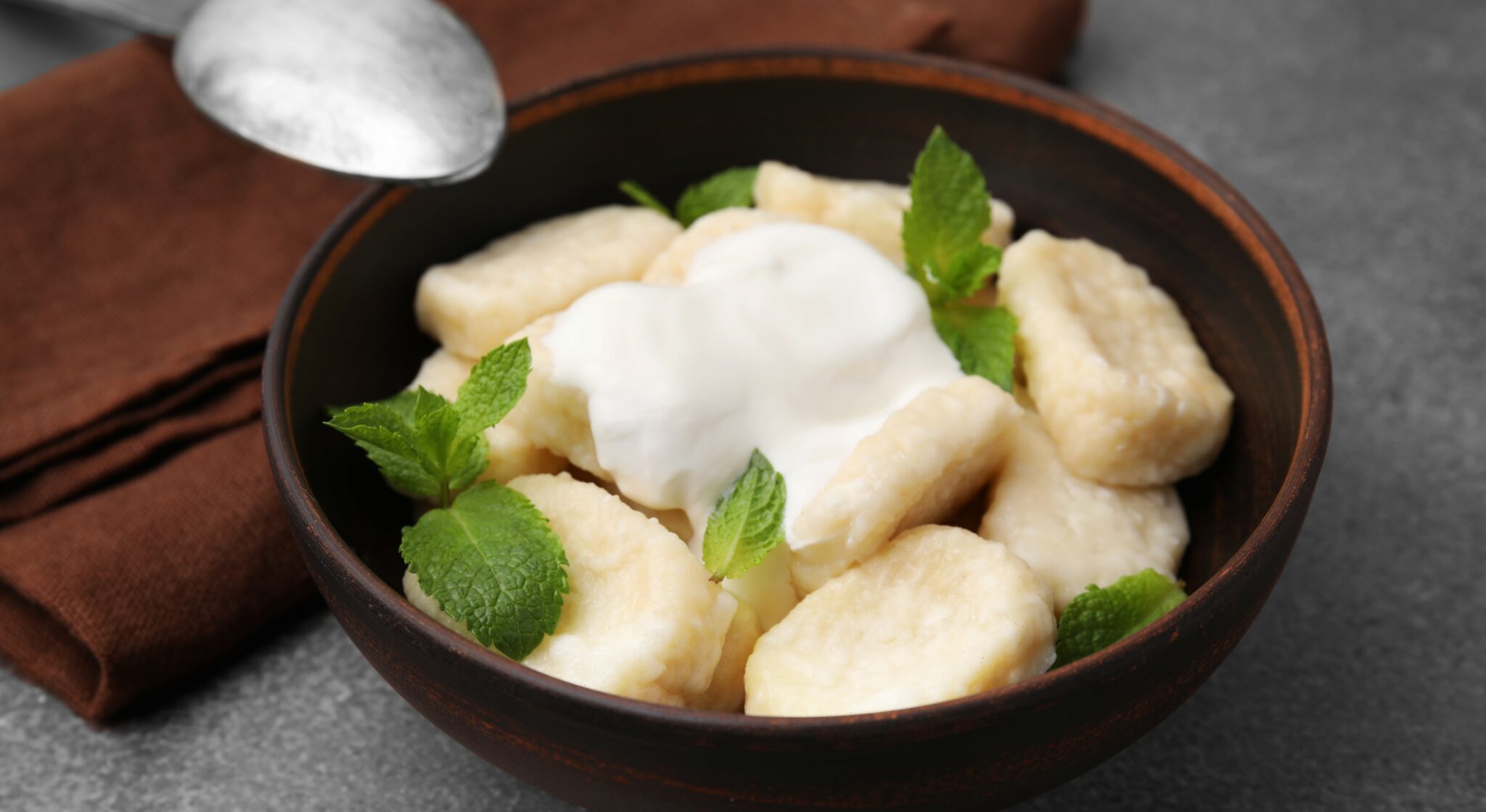 Bowl of tasty lazy dumplings with sour cream and mint leaves on brown table